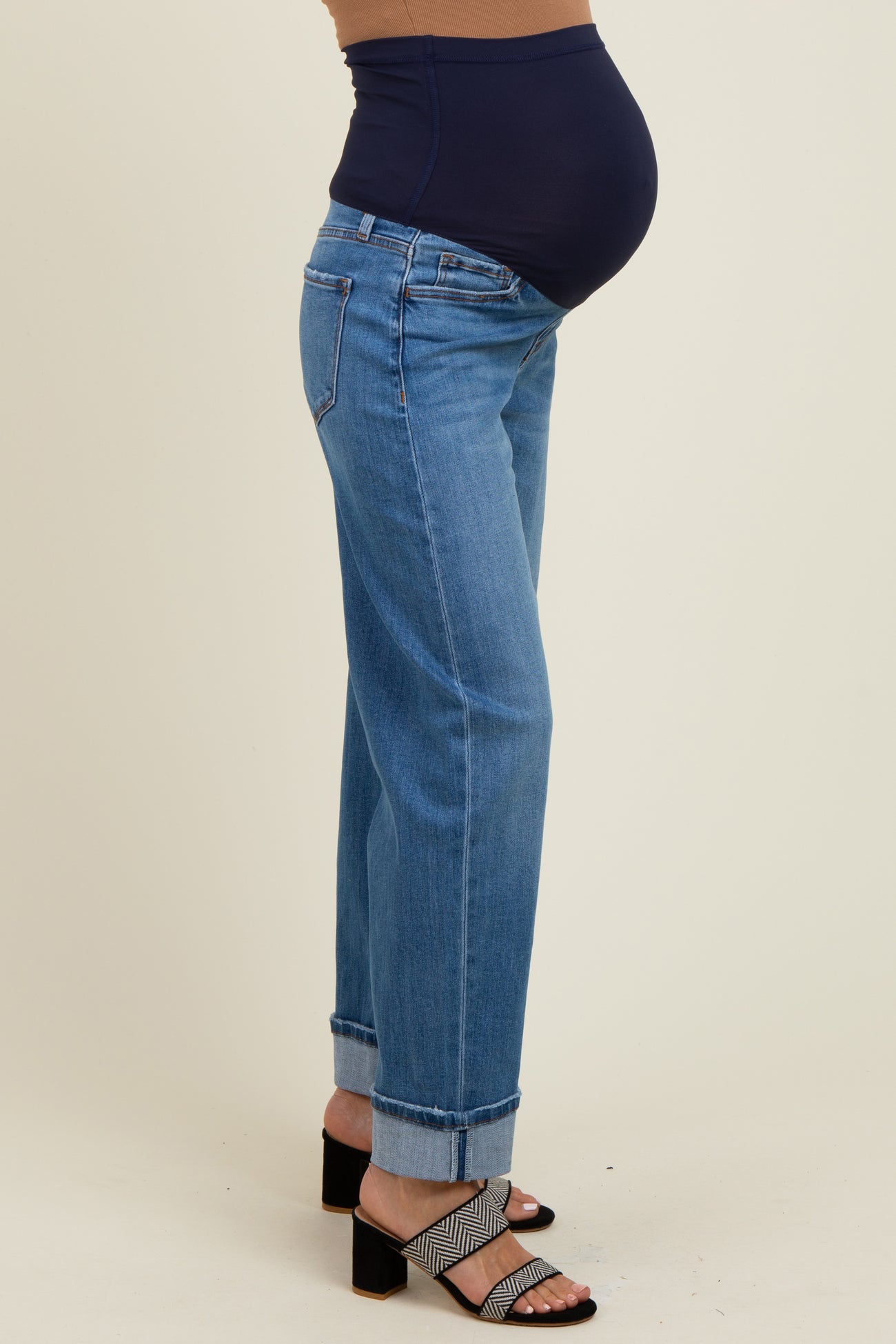 woman wearing light blue maternity jeans with a dark blue belly band, showcasing her baby bump and paired with black and white heeled sandals