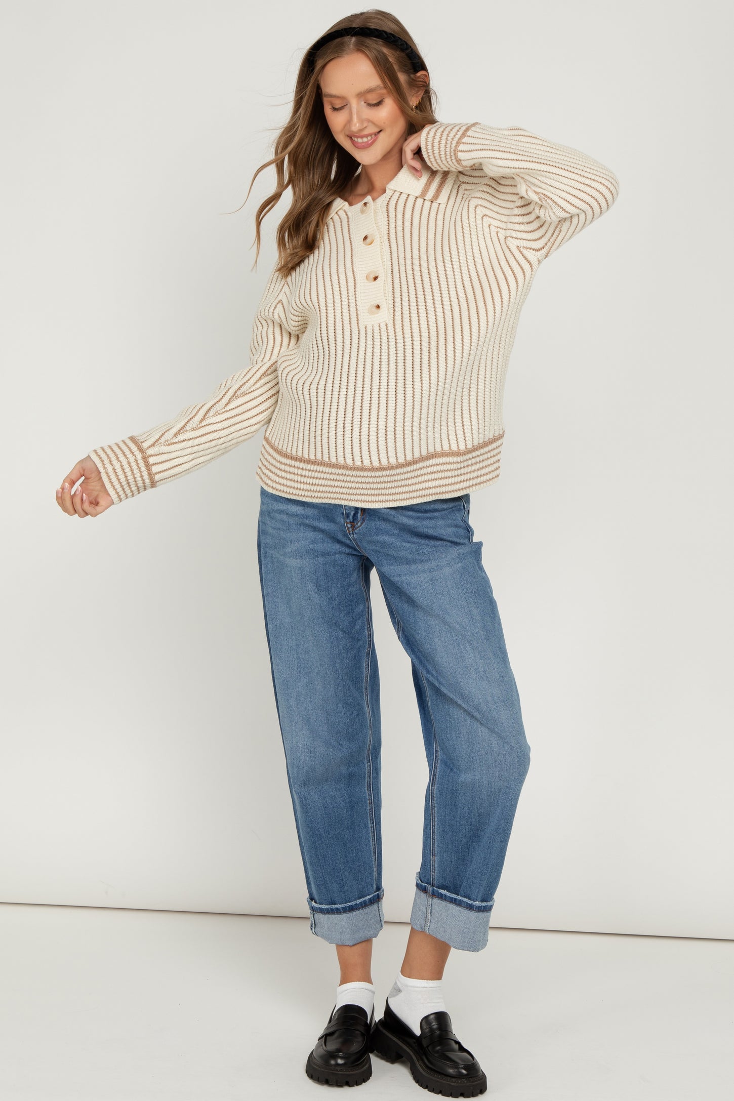 woman wearing a cream and beige striped maternity sweater with buttons, paired with rolled-up blue jeans