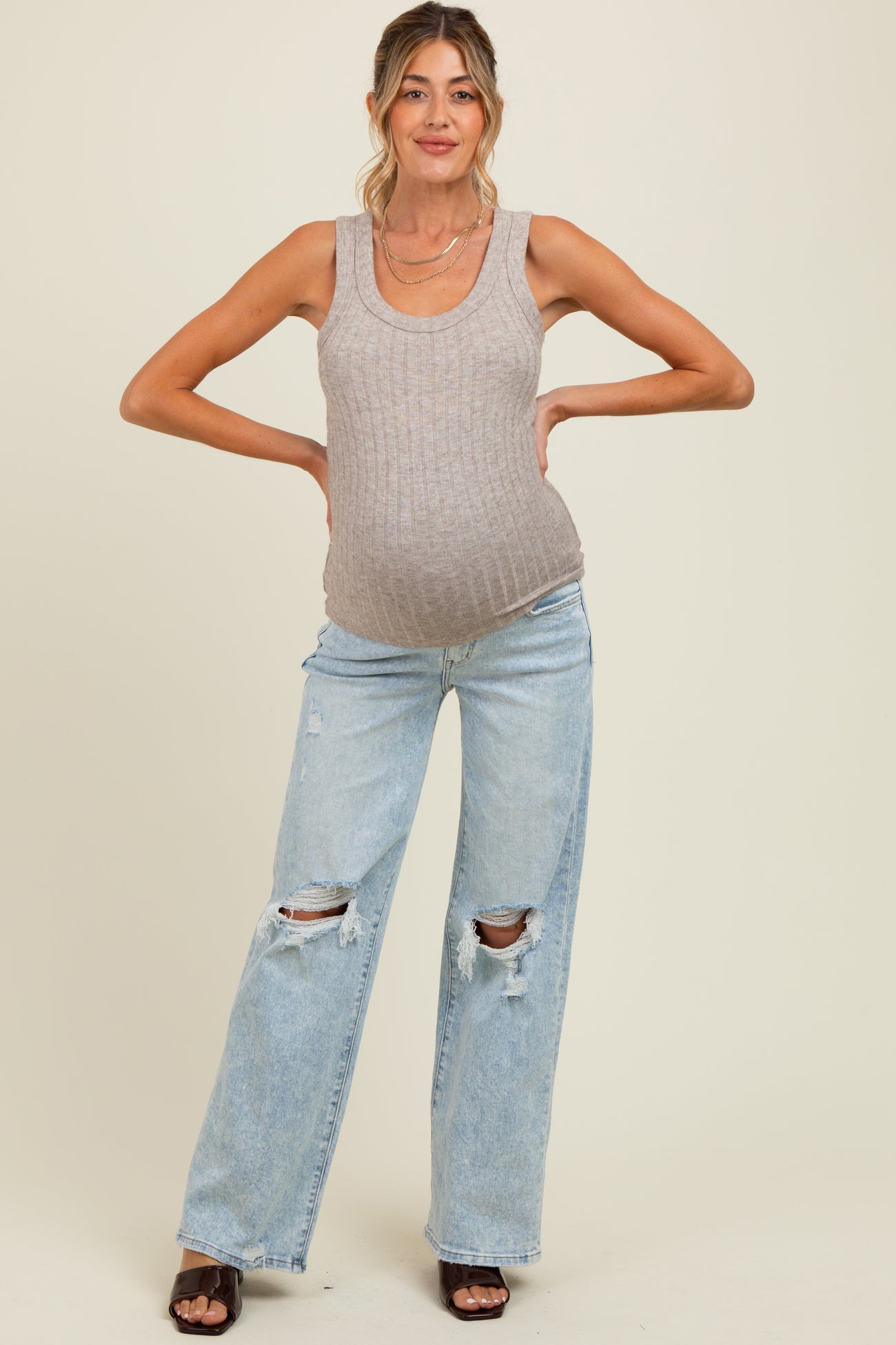 woman wearing a beige ribbed maternity tank top and distressed light blue jeans, showing her baby bump.
