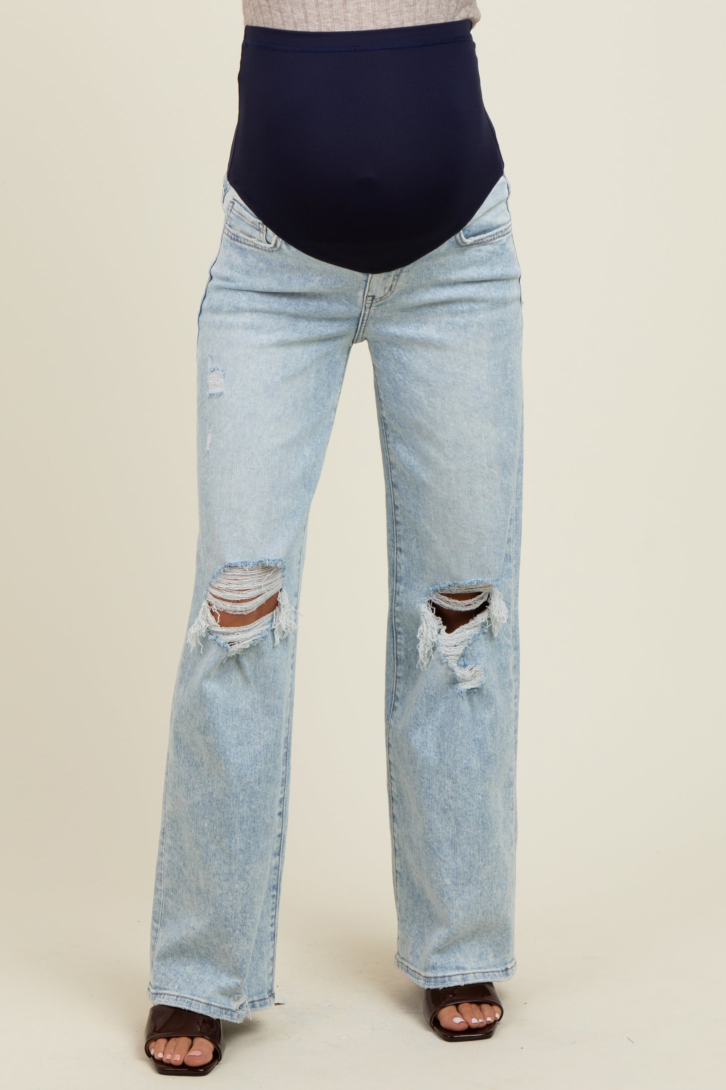 woman wearing light blue distressed maternity jeans with a navy blue over-the-bump waistband and no visible baby bump
