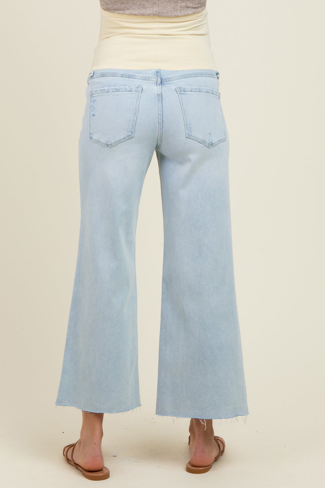 woman wearing light blue maternity wide leg jeans with a beige belly band visible at the waist