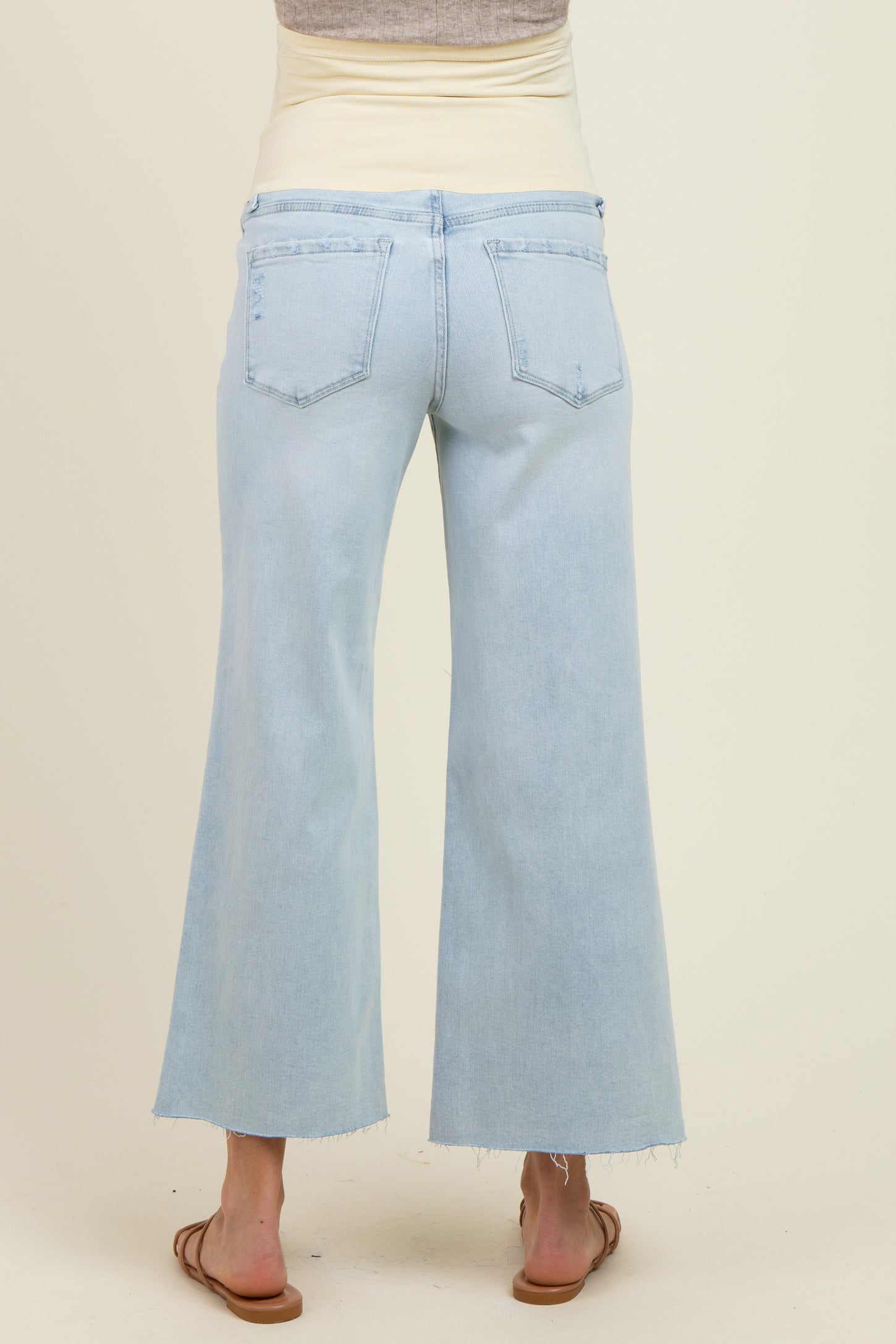 woman wearing light blue maternity wide leg jeans with a beige belly band visible at the waist