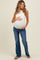woman wearing a white maternity tank top and blue flared maternity jeans, gently holding her baby bump