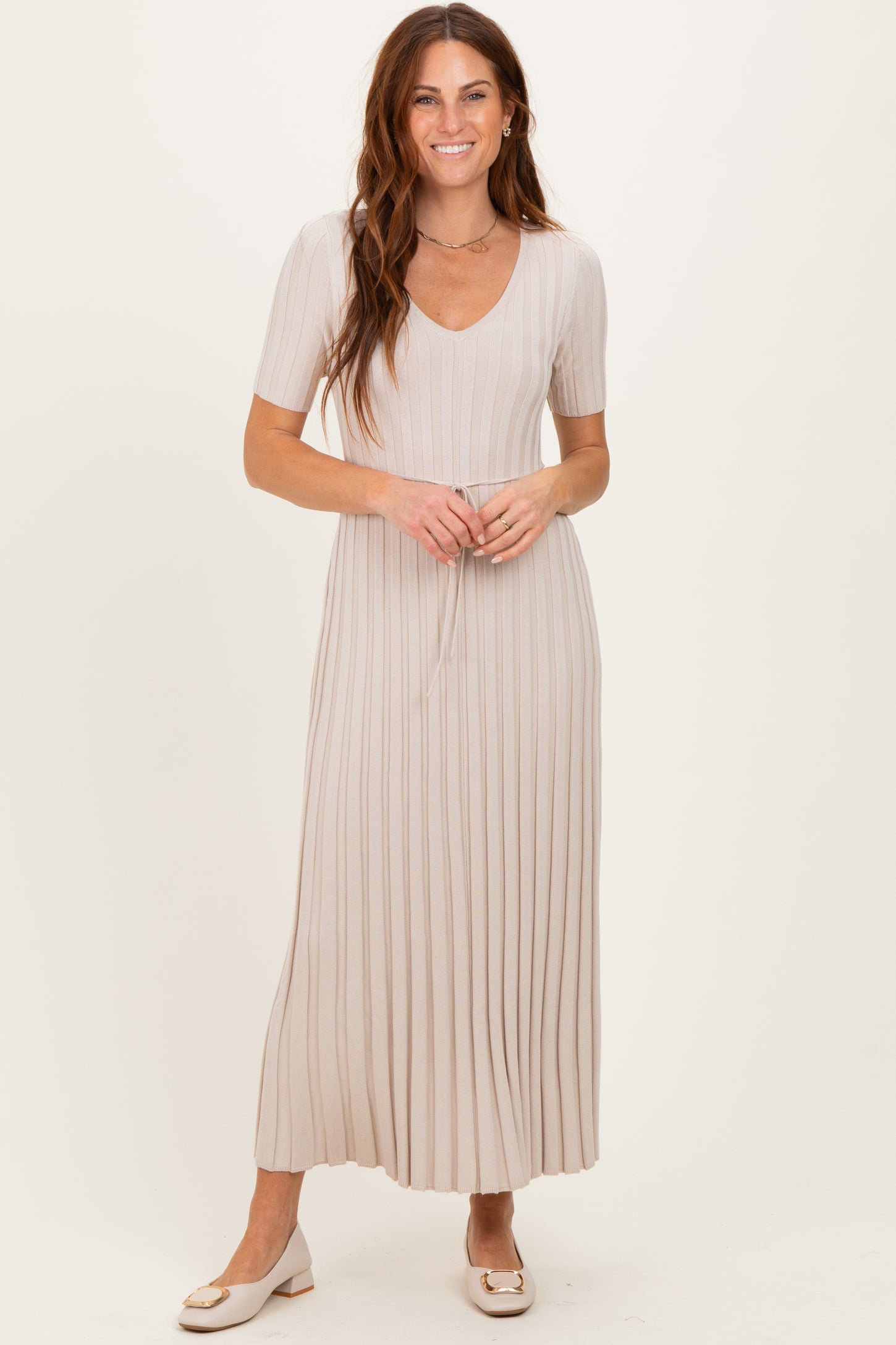 woman wearing a light beige pleated maxi dress with short sleeves and a tie waist detail