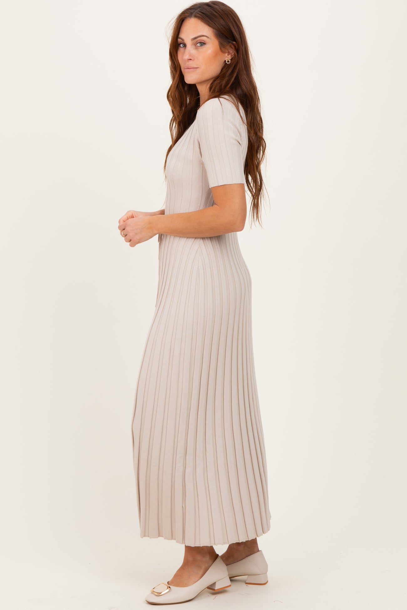 woman wearing a light beige ribbed maxi dress with short sleeves and side slits, paired with white heeled mules