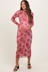 woman wearing a sheer pink floral maternity dress and holding her baby bump