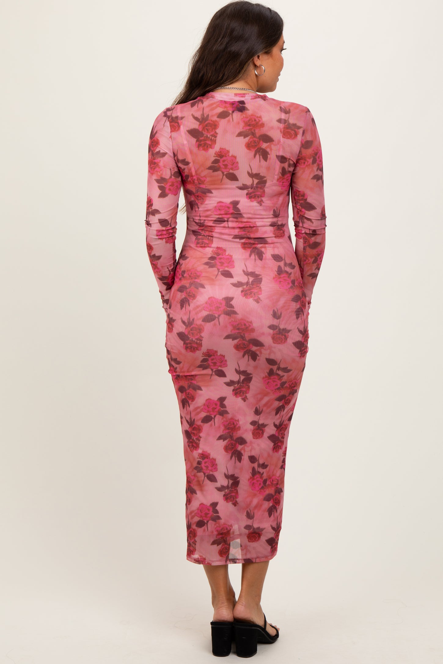 woman wearing a sheer pink floral maternity dress with long sleeves and a form-fitting silhouette