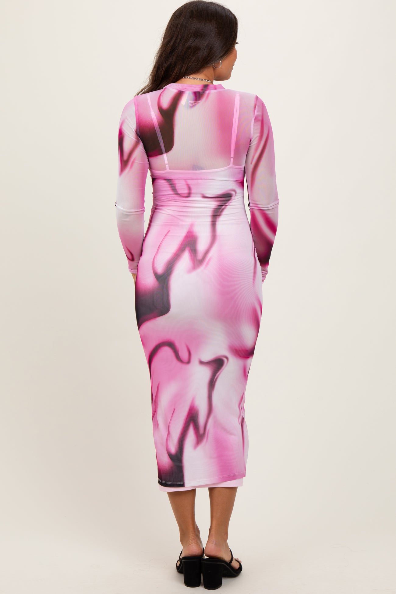 woman wearing a long sleeve pink and white abstract print maternity dress, showing a pregnant belly from the back