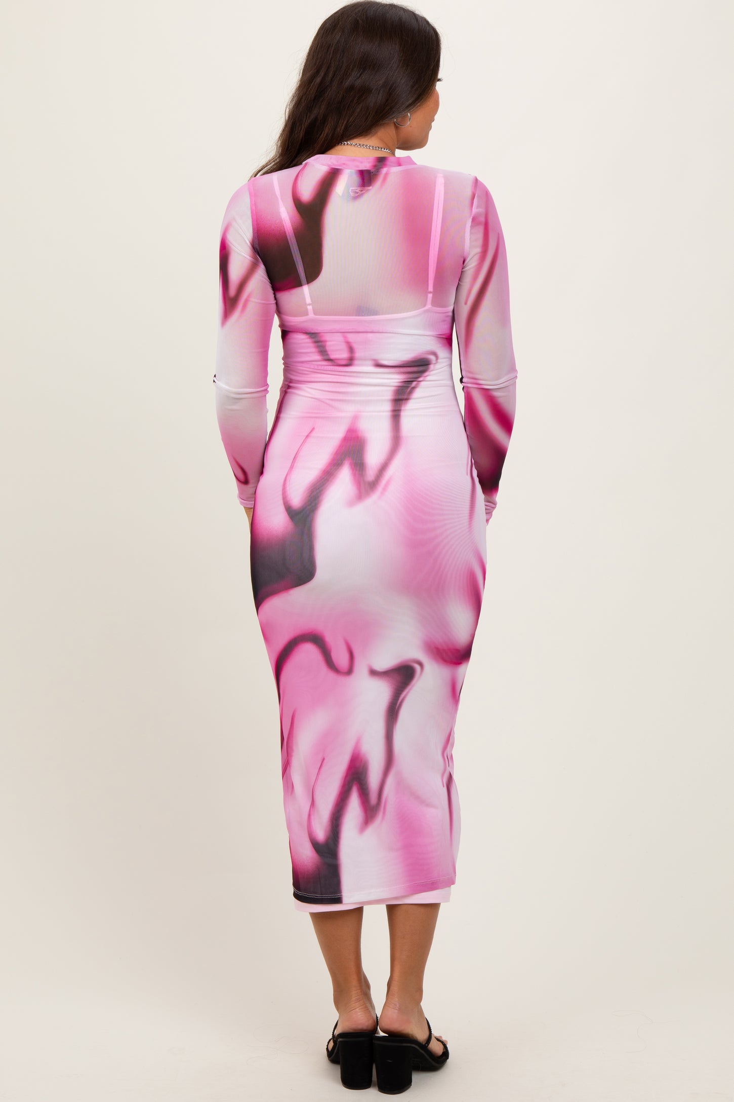 woman wearing a long sleeve pink and white abstract print maternity dress, showing a pregnant belly from the back