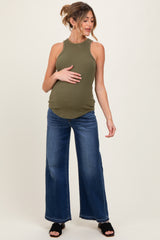 woman wearing a dark green ribbed maternity tank top and wide leg jeans, holding her baby bump