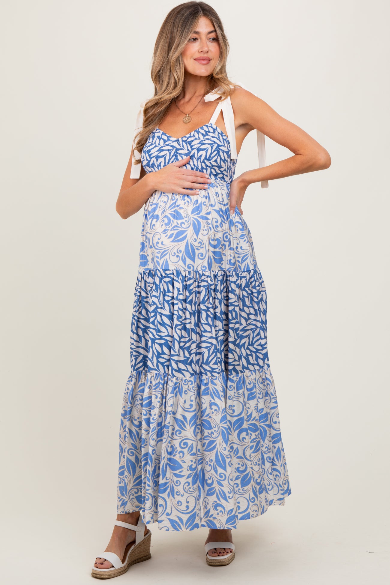 woman wearing a blue and white floral maternity maxi dress with tie straps and holding her baby bump