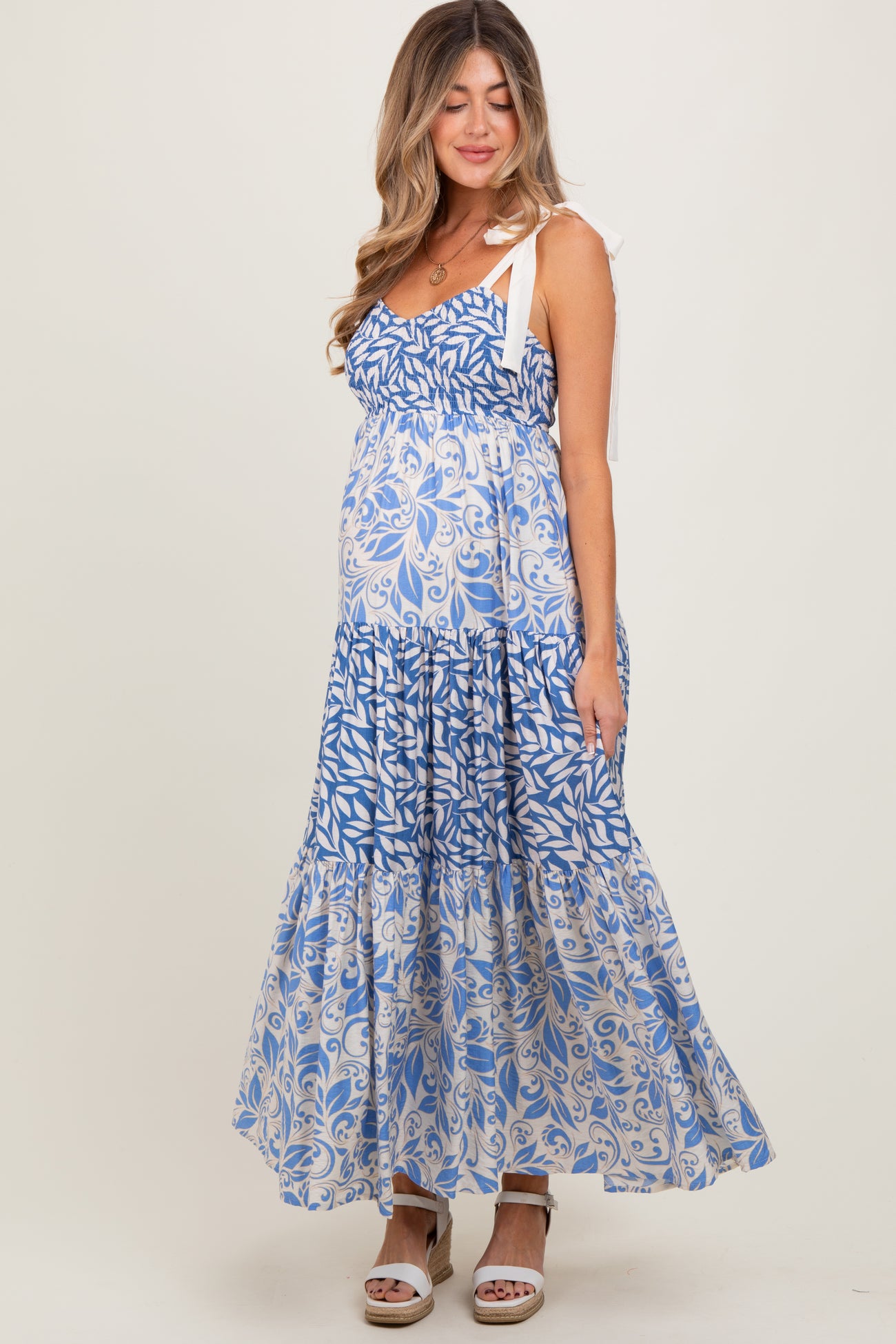 woman wearing a blue and white floral maternity maxi dress with tie straps and a visible baby bump