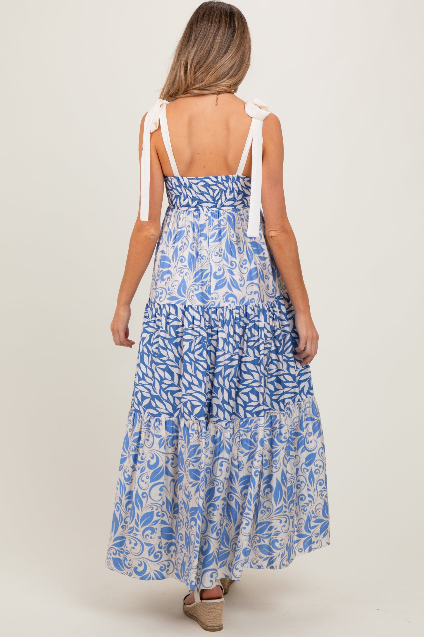 woman wearing a blue floral print maternity maxi dress with tie straps and tiered ruffles, showing her back
