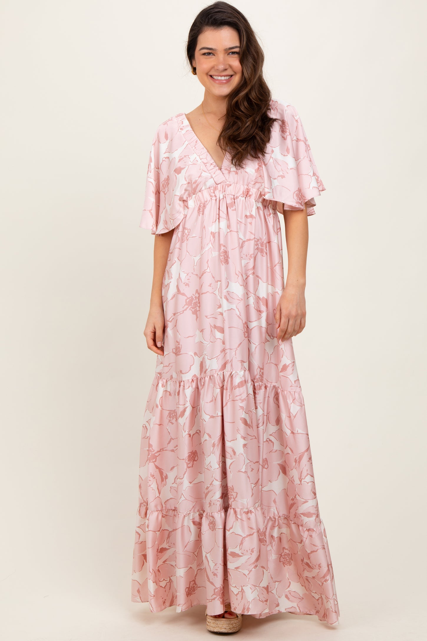 woman wearing a pink floral maxi dress with short flutter sleeves and a tiered ruffle hem
