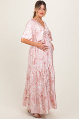 woman wearing a pink floral maternity maxi dress with ruffled tiers and a matching cardigan, holding her baby bump
