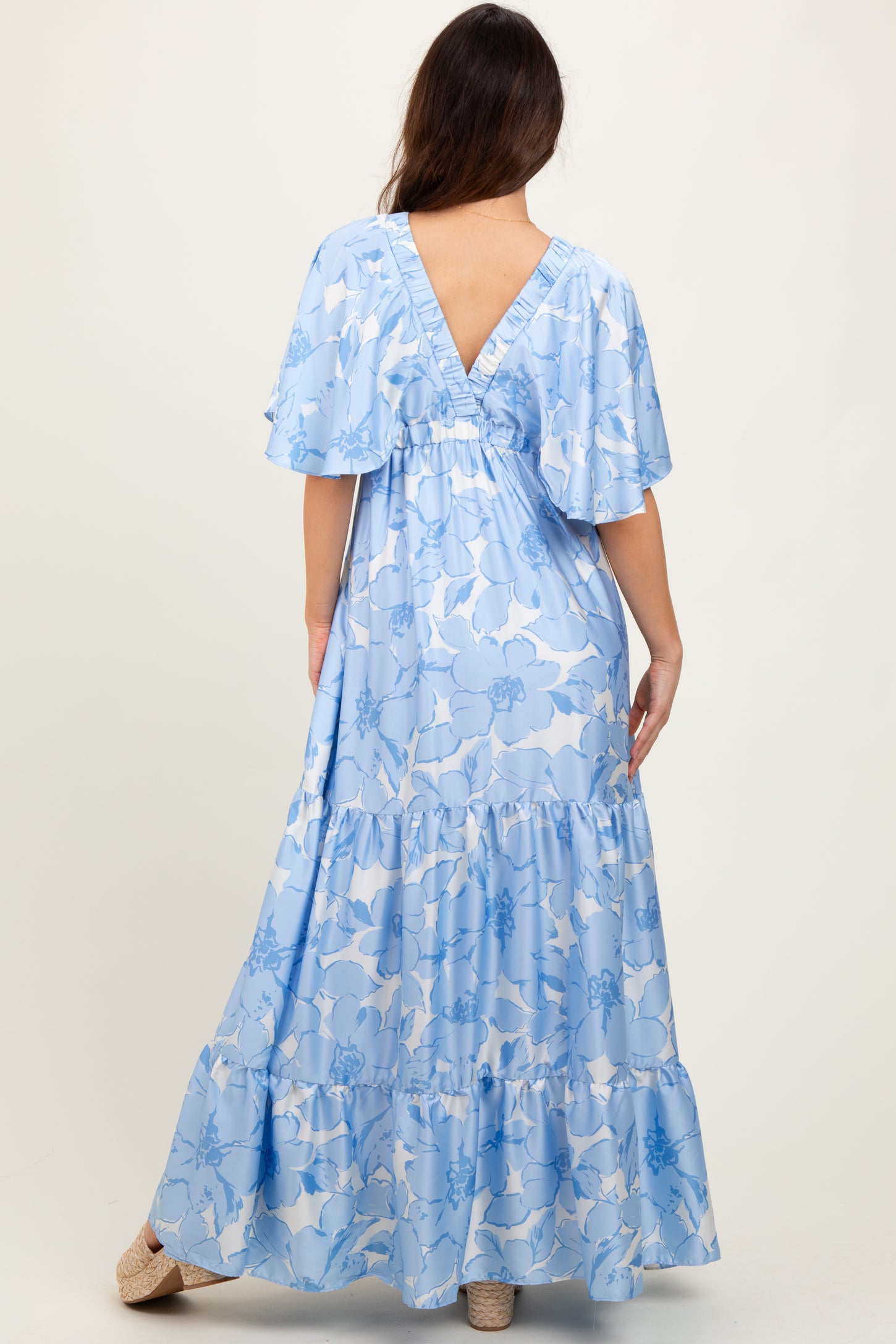 woman wearing a blue floral maxi dress with flutter sleeves and a v-back design