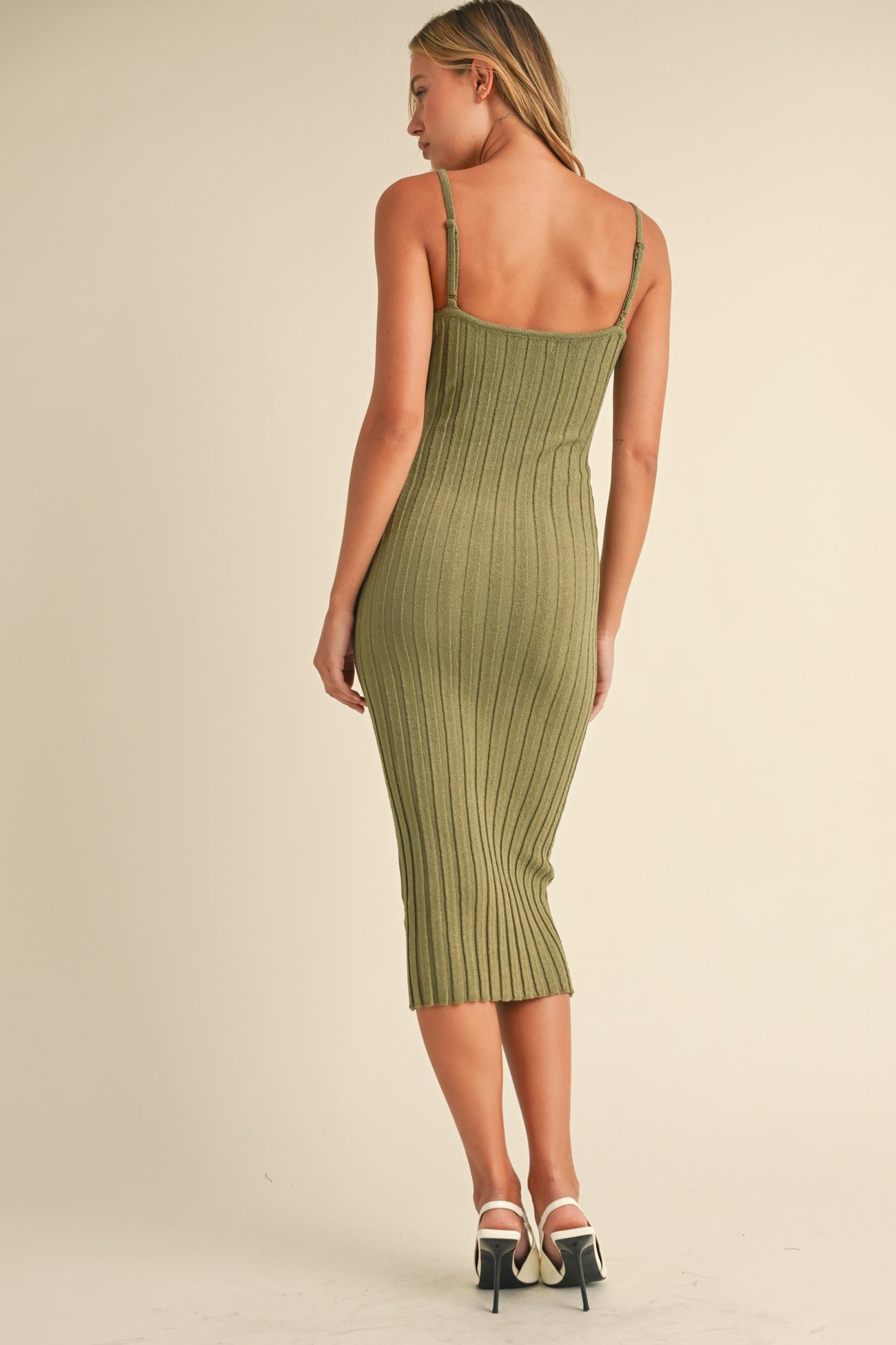 woman wearing an olive green ribbed midi dress with thin straps, styled with white heels, seen from the back