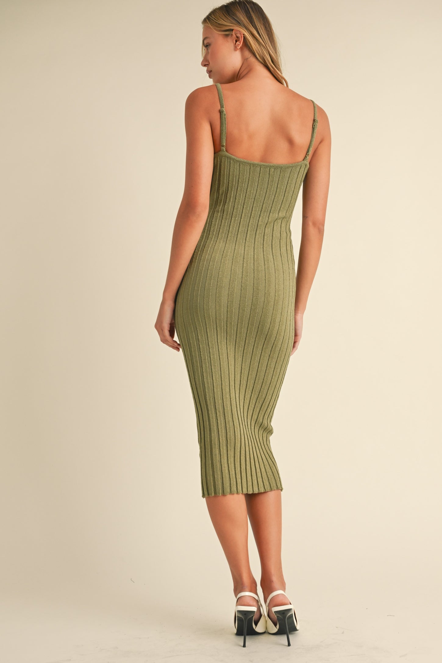 woman wearing an olive green ribbed midi dress with thin straps, styled with white heels, seen from the back