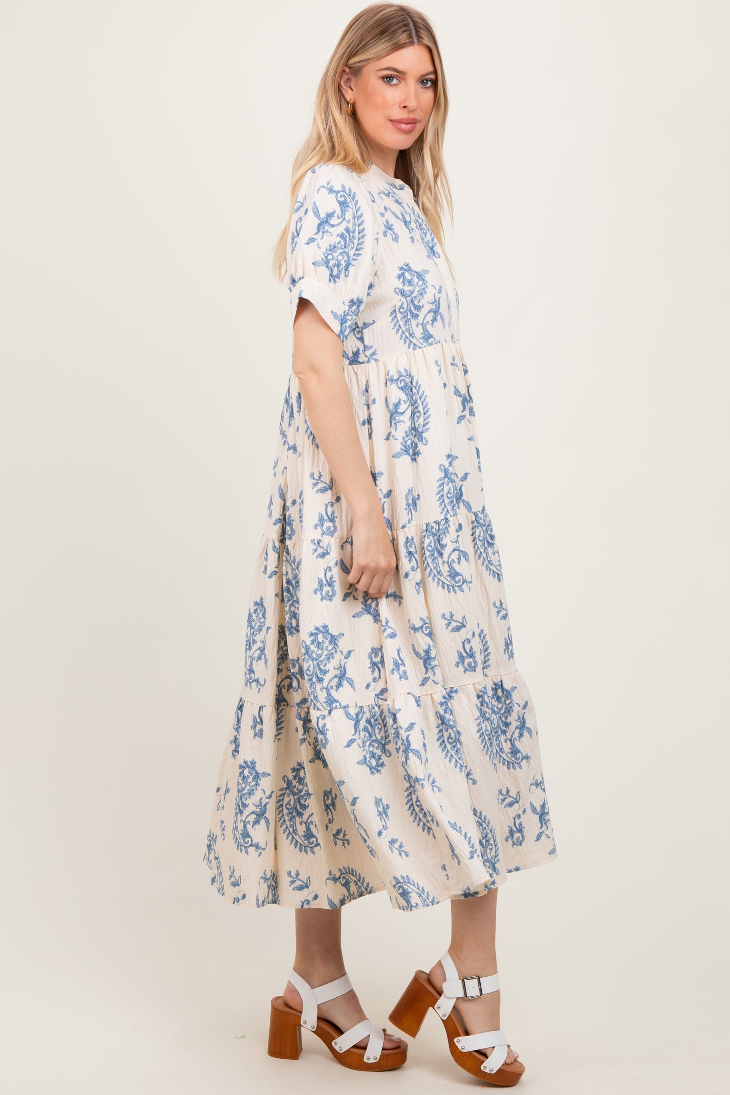 woman wearing a cream and blue floral print maxi dress with short sleeves and a tiered design