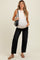 woman wearing a white maternity tank top and black jeans, holding a black bag, showing her baby bump
