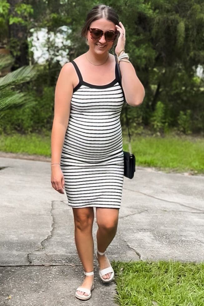 woman wearing a black and white striped maternity dress and showcasing her baby bump while walking outdoors