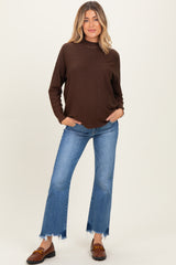 woman wearing a brown long sleeve maternity sweater with a loose fit and pair of flared jeans