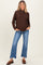 woman wearing a brown long sleeve maternity sweater with a loose fit and pair of flared jeans