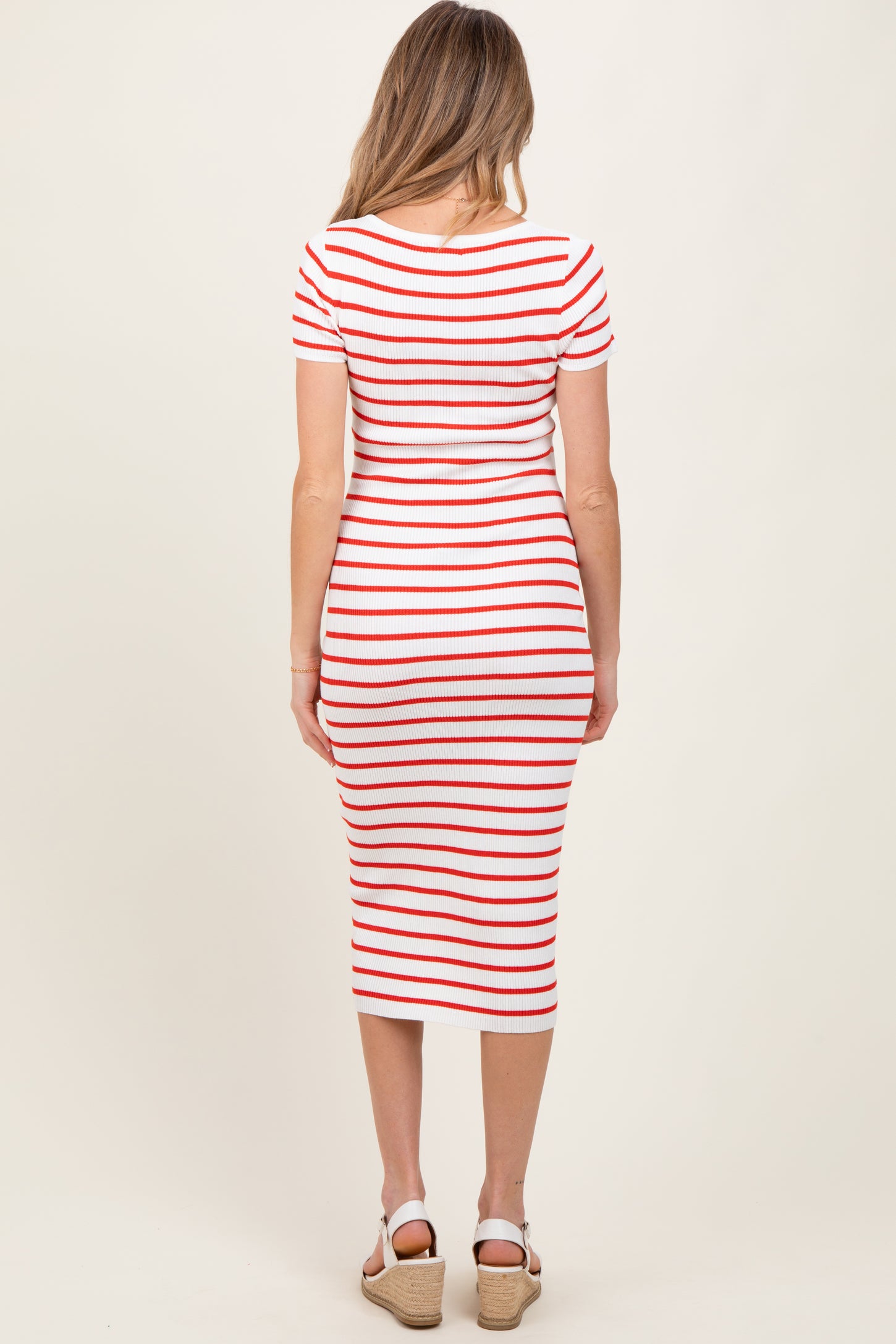 woman wearing a red and white striped maternity dress, showing a fitted style and knee-length cut from the back