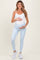 woman wearing a white maternity tank top and light blue leggings, holding her baby bump