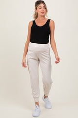 woman wearing a black tank top and cream maternity joggers with a full belly panel, styled with white sneakers