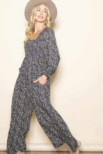 woman wearing a floral print long sleeve jumpsuit with pockets and a wide-brimmed hat