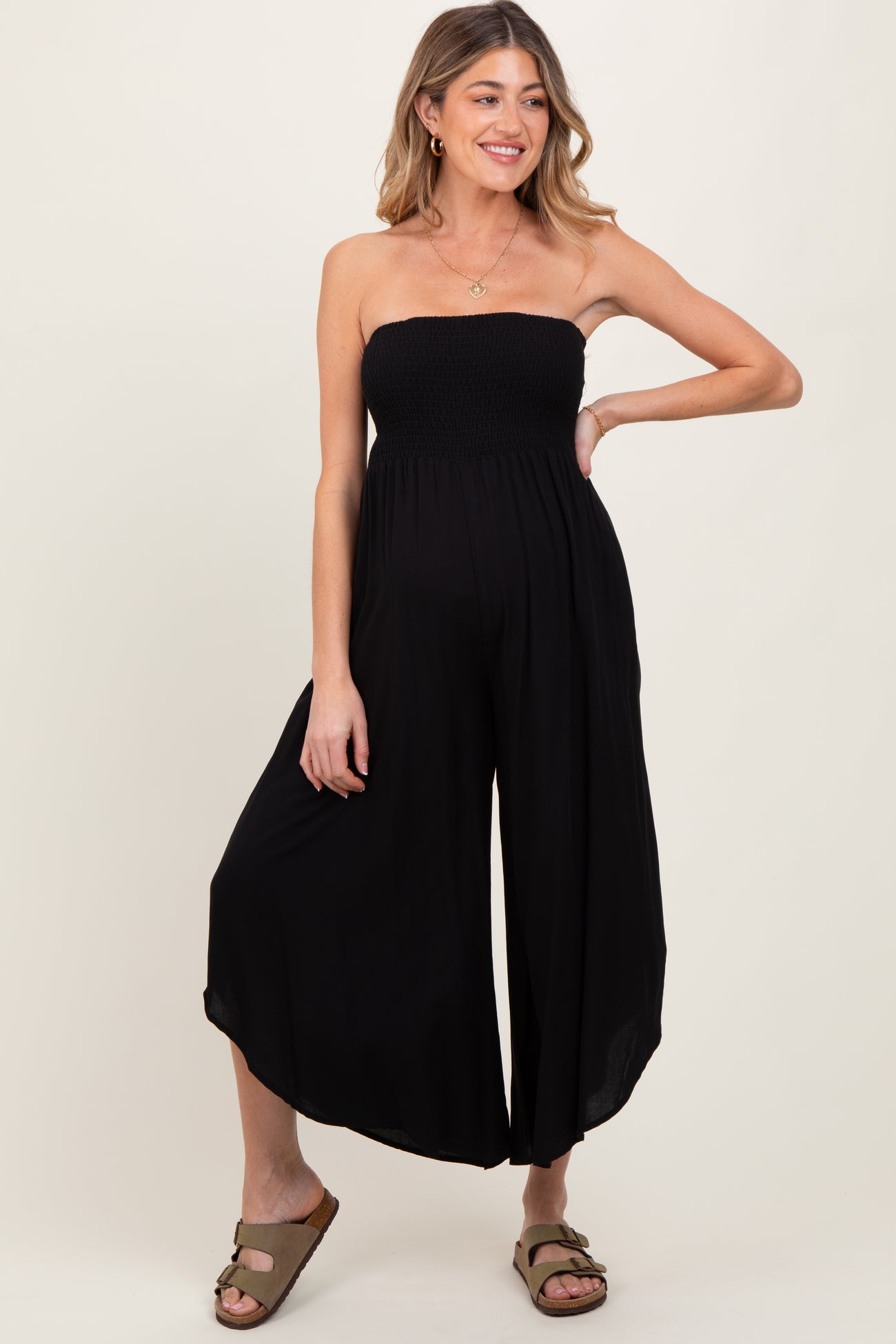 woman wearing a black strapless maternity jumpsuit with a smocked bodice and wide leg pants, showing her baby bump