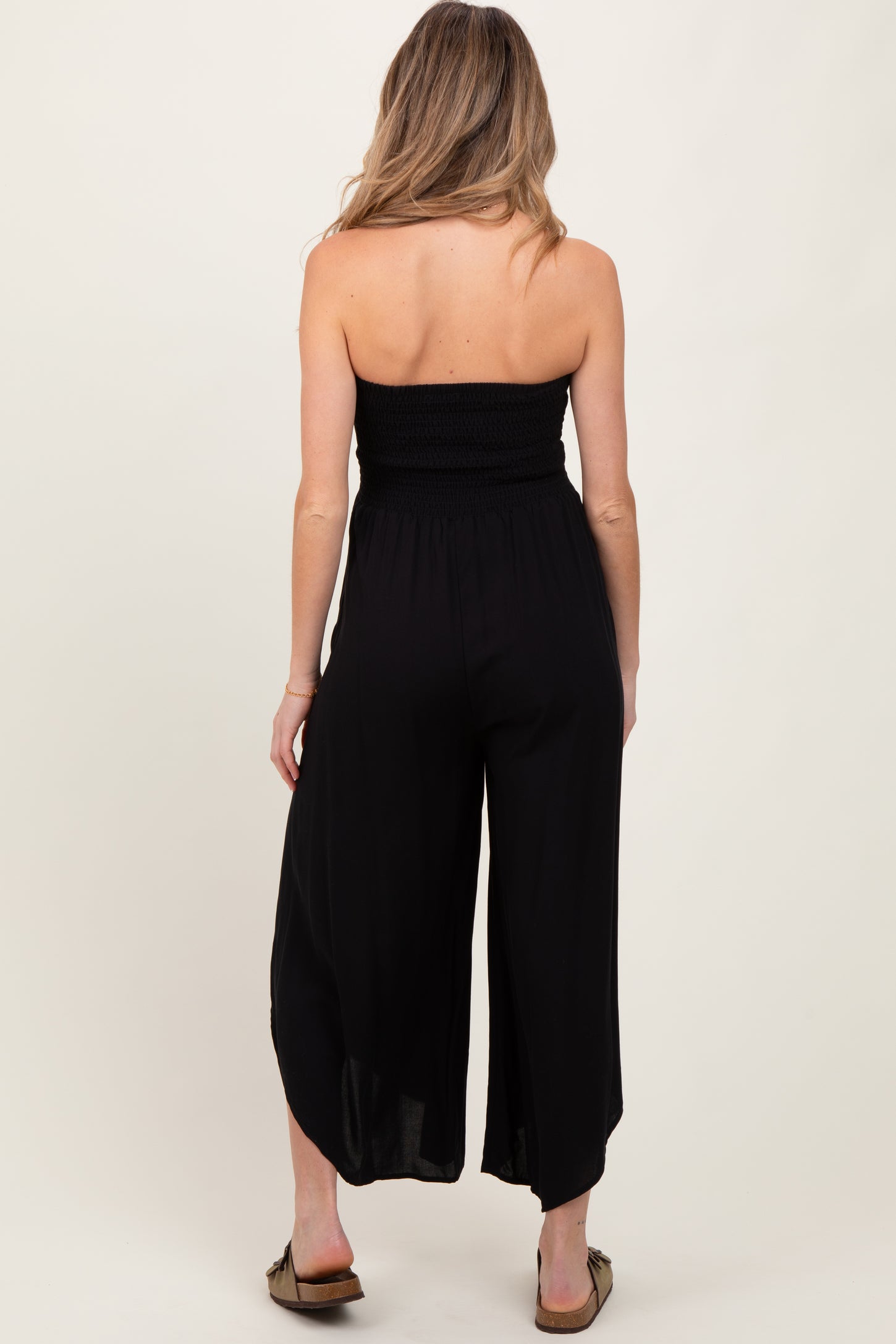 woman wearing a black strapless maternity jumpsuit, showing a smocked bodice and wide-leg design from the back