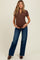woman wearing a brown short sleeve maternity top with buttons and blue wide leg jeans, holding her baby bump