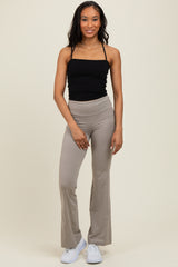 woman wearing a black spaghetti strap top and beige flared yoga pants, standing and smiling