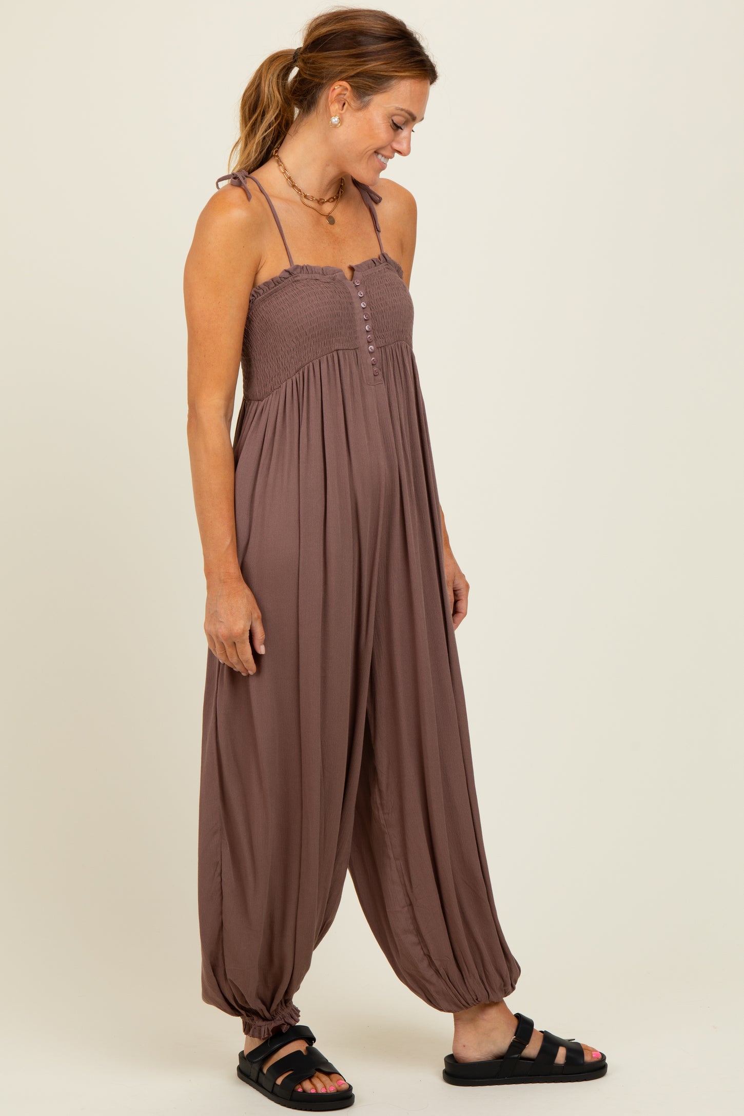 woman wearing a brown sleeveless jumpsuit with a smocked bodice and wide legs, styled with black sandals
