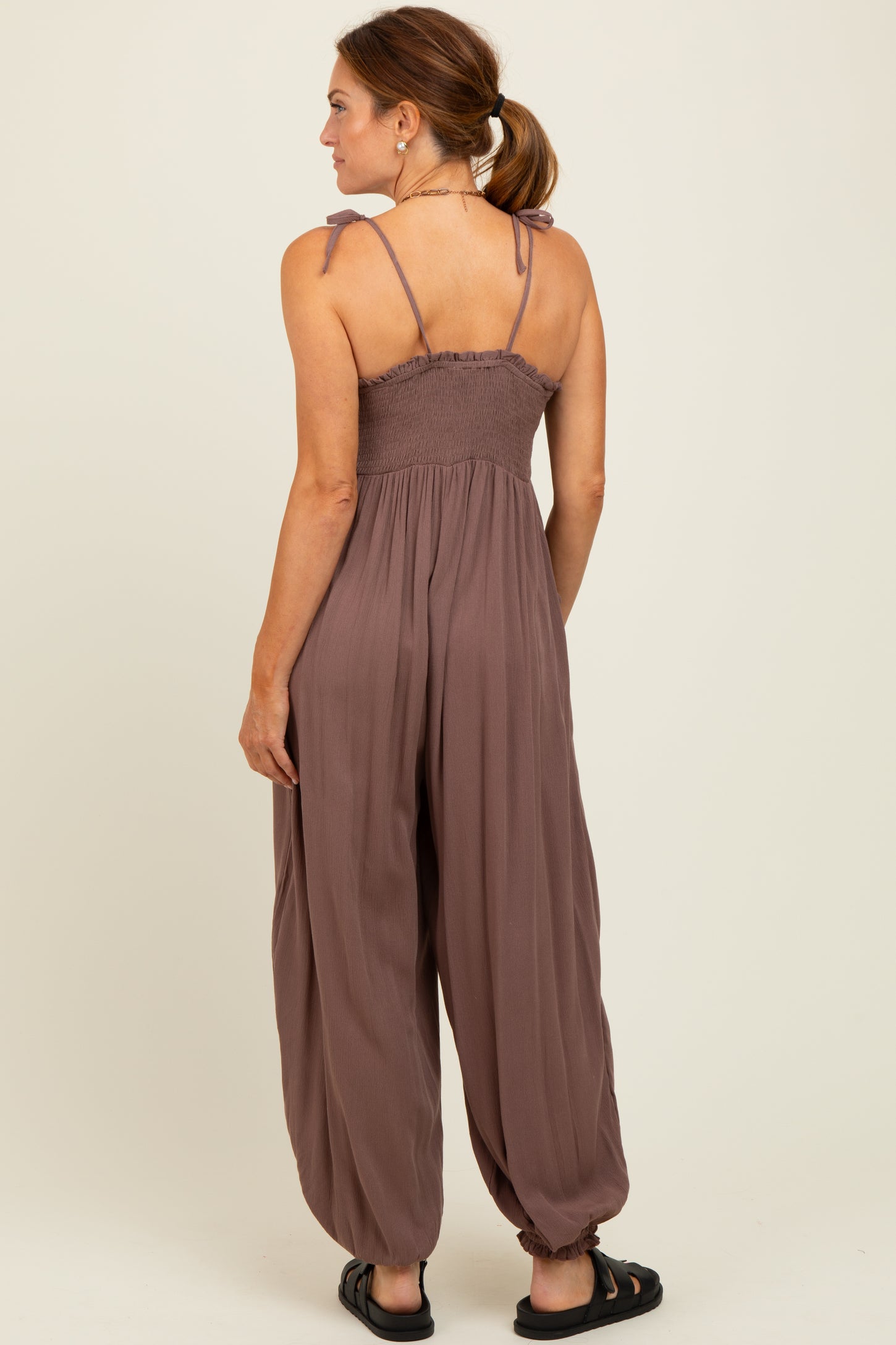 woman wearing a back view of a mauve jumpsuit with smocked bodice and adjustable straps