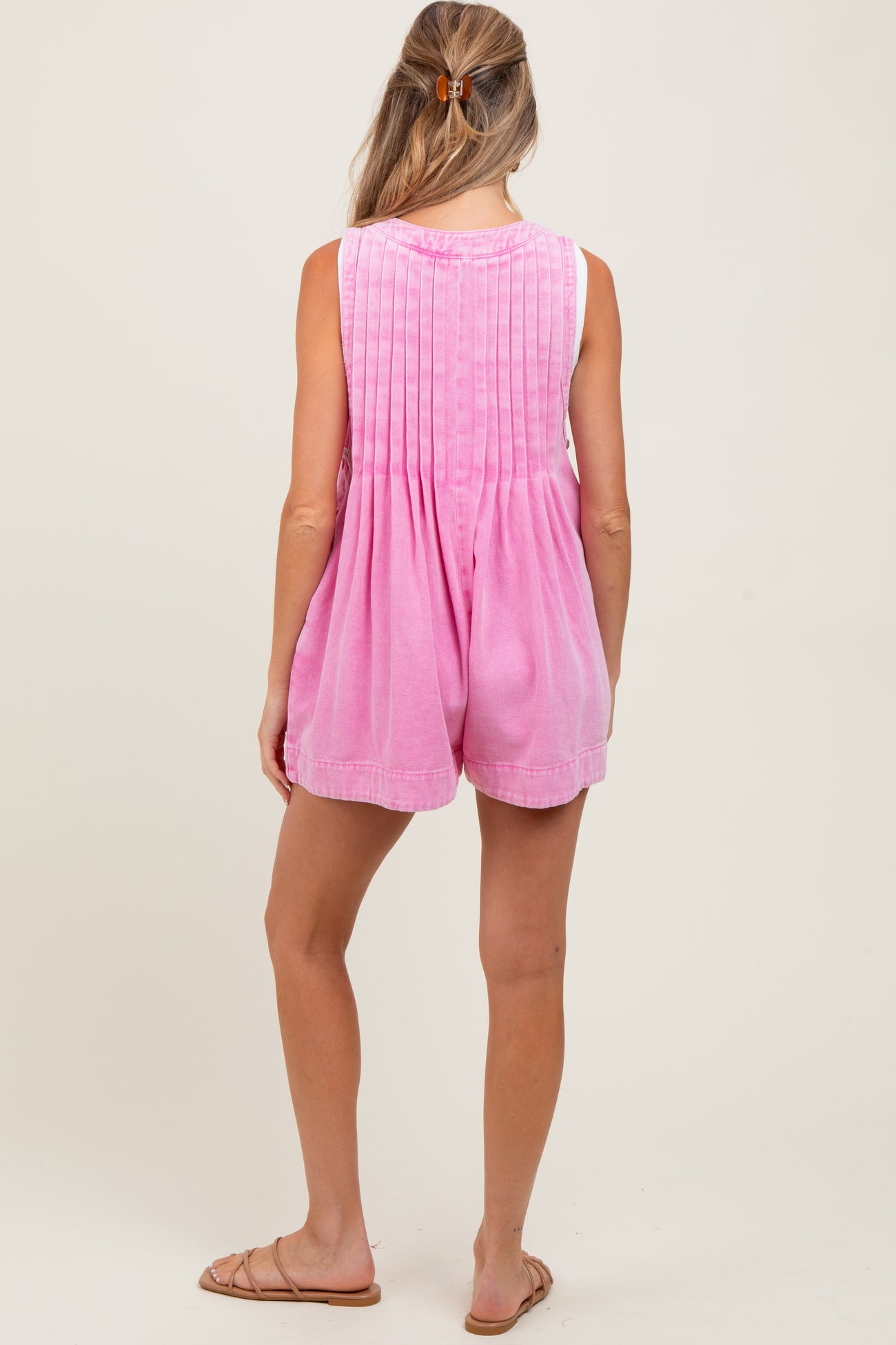 woman wearing a pink maternity romper with pleated back details, standing with her back to the camera