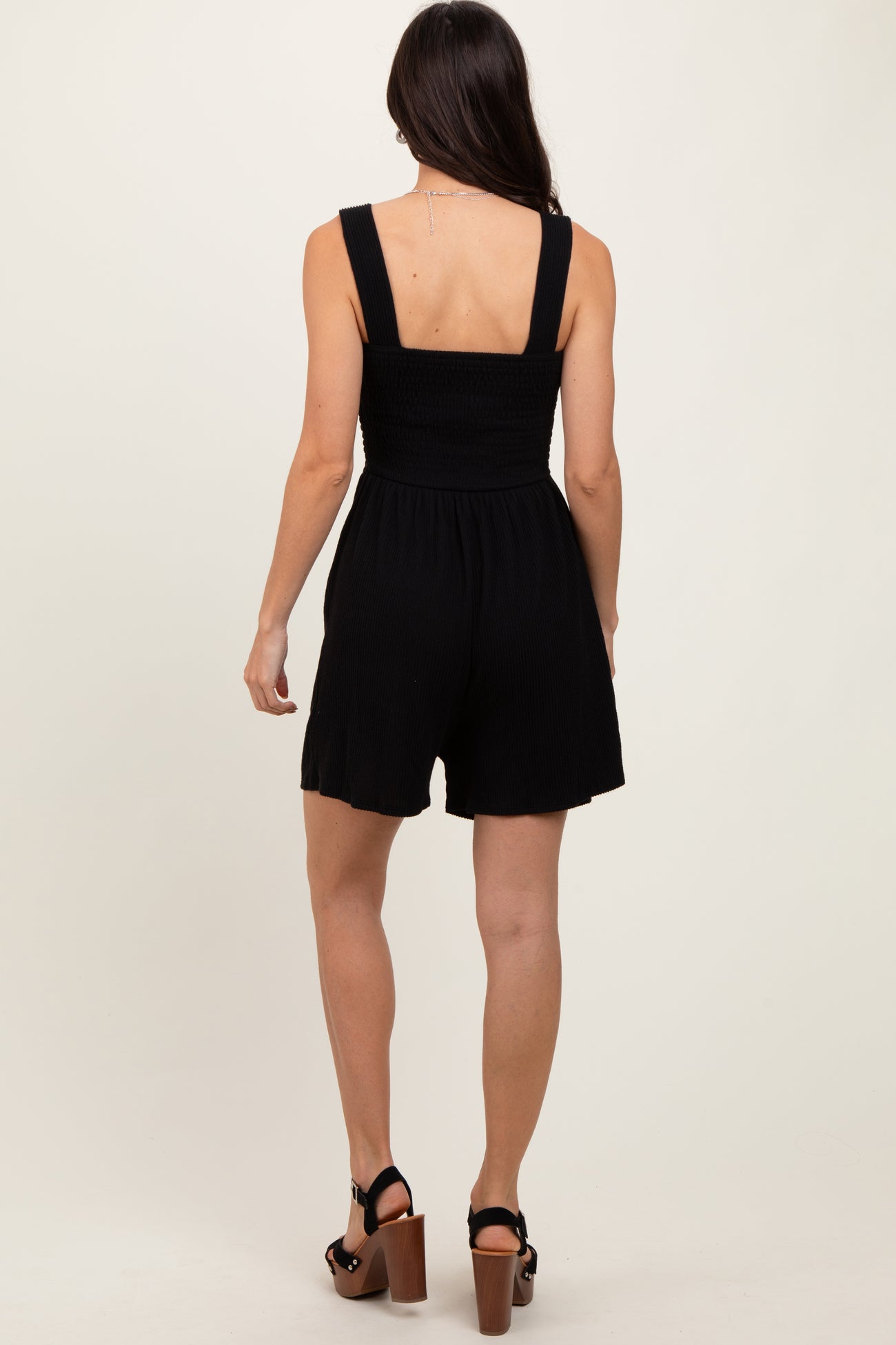 woman wearing a black smocked back jumpsuit with thick straps and a relaxed fit, showing the back view