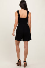 woman wearing a black smocked back jumpsuit with thick straps and a relaxed fit, showing the back view