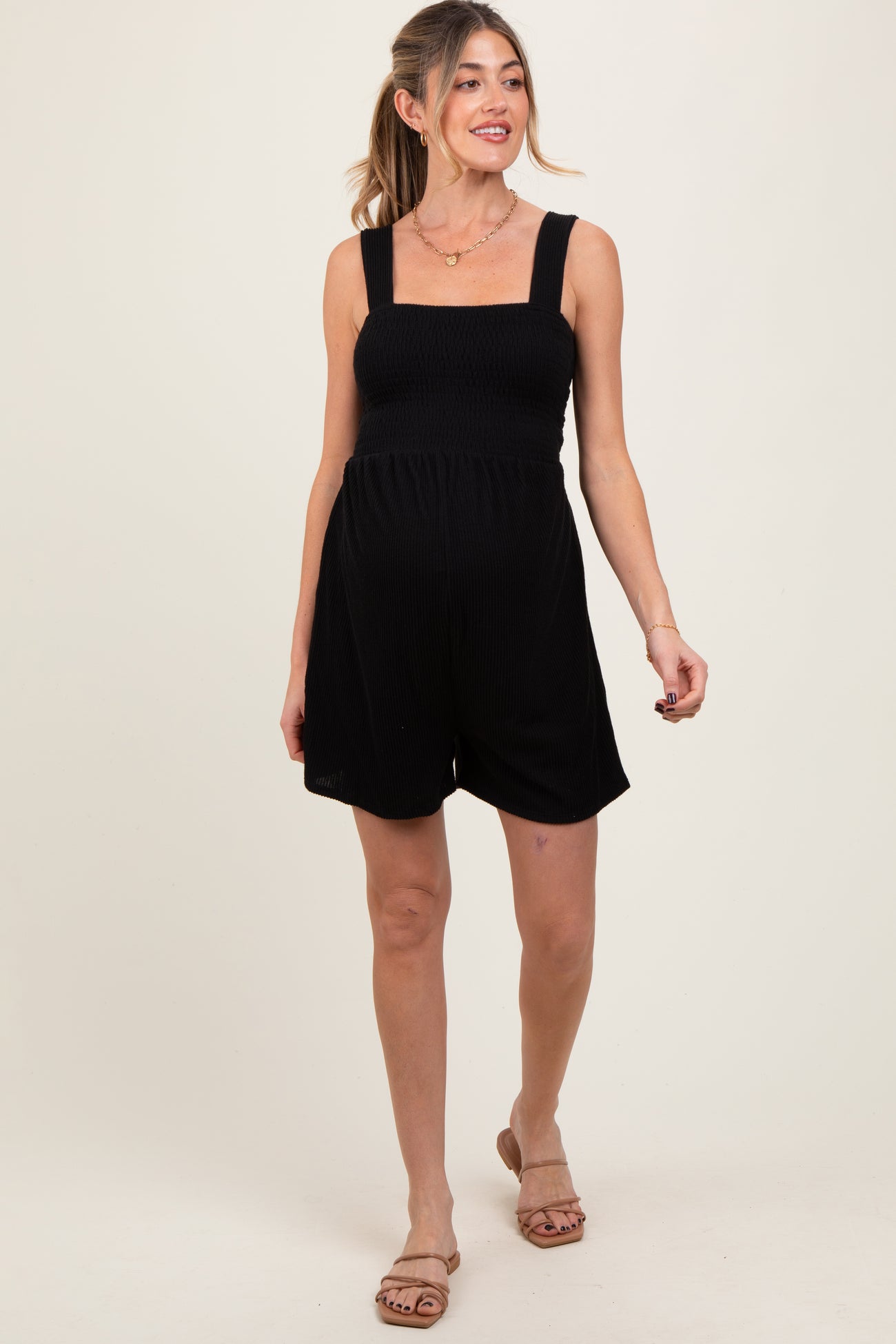 woman wearing a black maternity romper with a smocked bodice and wide straps, showcasing her baby bump