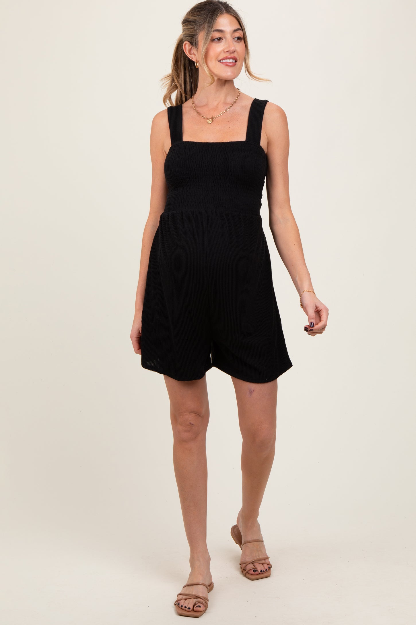 woman wearing a black maternity romper with a smocked bodice and wide straps, showcasing her baby bump