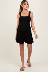 woman wearing a black maternity romper with a smocked bodice and wide straps, showcasing her baby bump