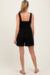 woman wearing a black maternity romper with smocked detailing, showing the back view