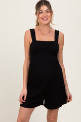 woman wearing a black smocked maternity romper with wide straps and a relaxed fit, showing her baby bump