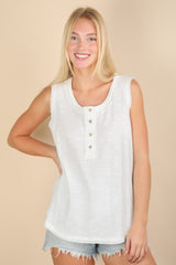 woman wearing a white sleeveless top with buttons and a rounded hem, paired with denim shorts