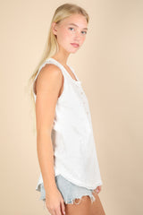 woman wearing a white sleeveless button-up top and denim shorts, standing sideways against a neutral background