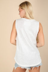 woman wearing a white sleeveless top with a round hem and distressed denim shorts