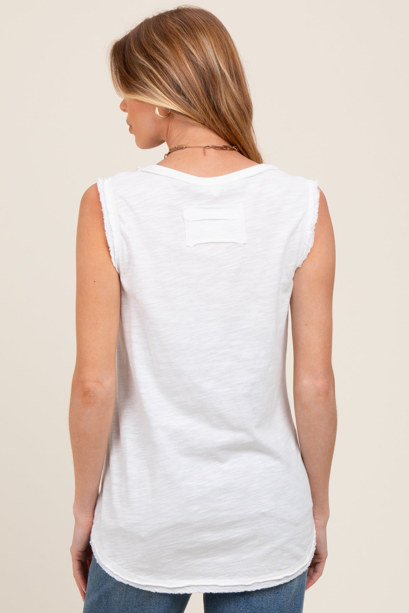 woman wearing a white maternity tank top with a raw hem and back detail, showcasing a relaxed fit and slightly longer length