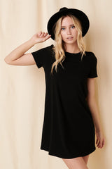woman wearing a black short sleeve ribbed dress and a black hat, posing against a light background